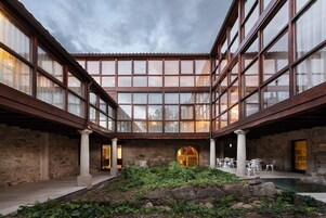 Un amplio patio con un muro de piedra, un arco central y una zona de estar con mesas y sillas.