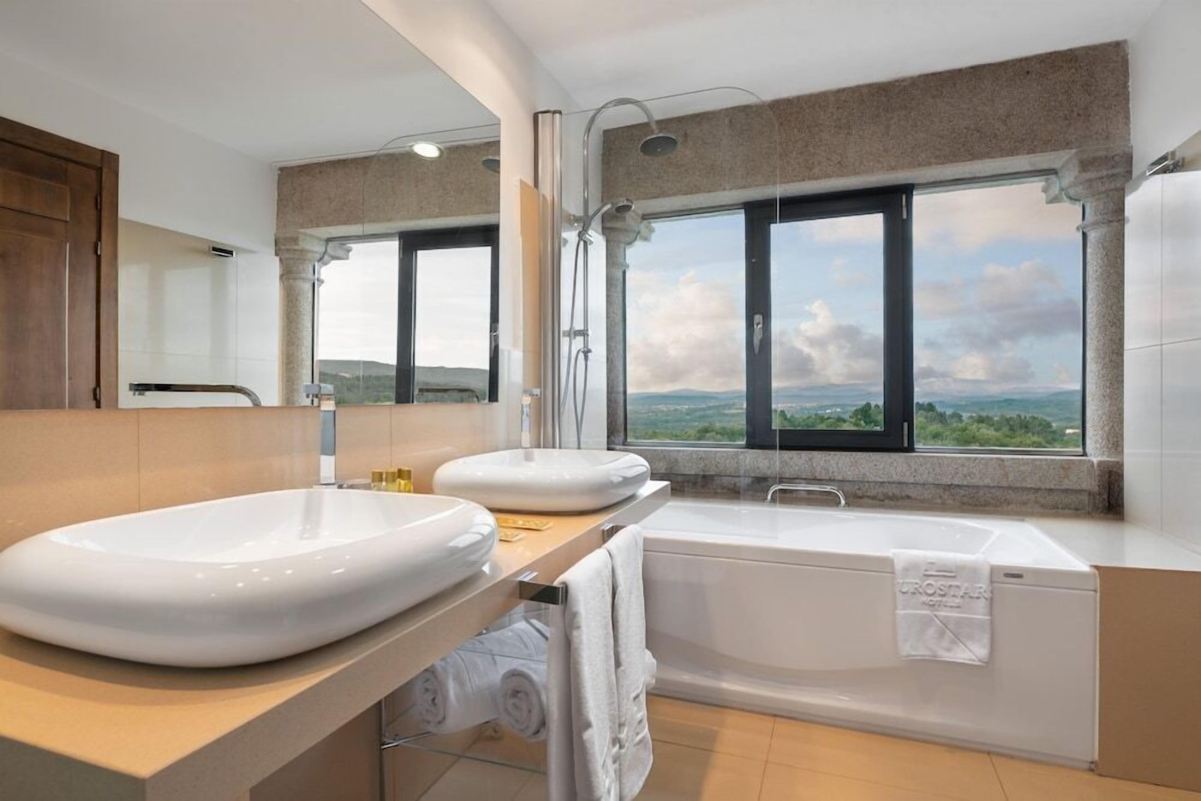 A modern bathroom with a large sink, a bathtub, and a window offering a scenic view.