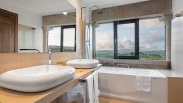 A modern bathroom with a large sink, a bathtub, and a window offering a scenic view.