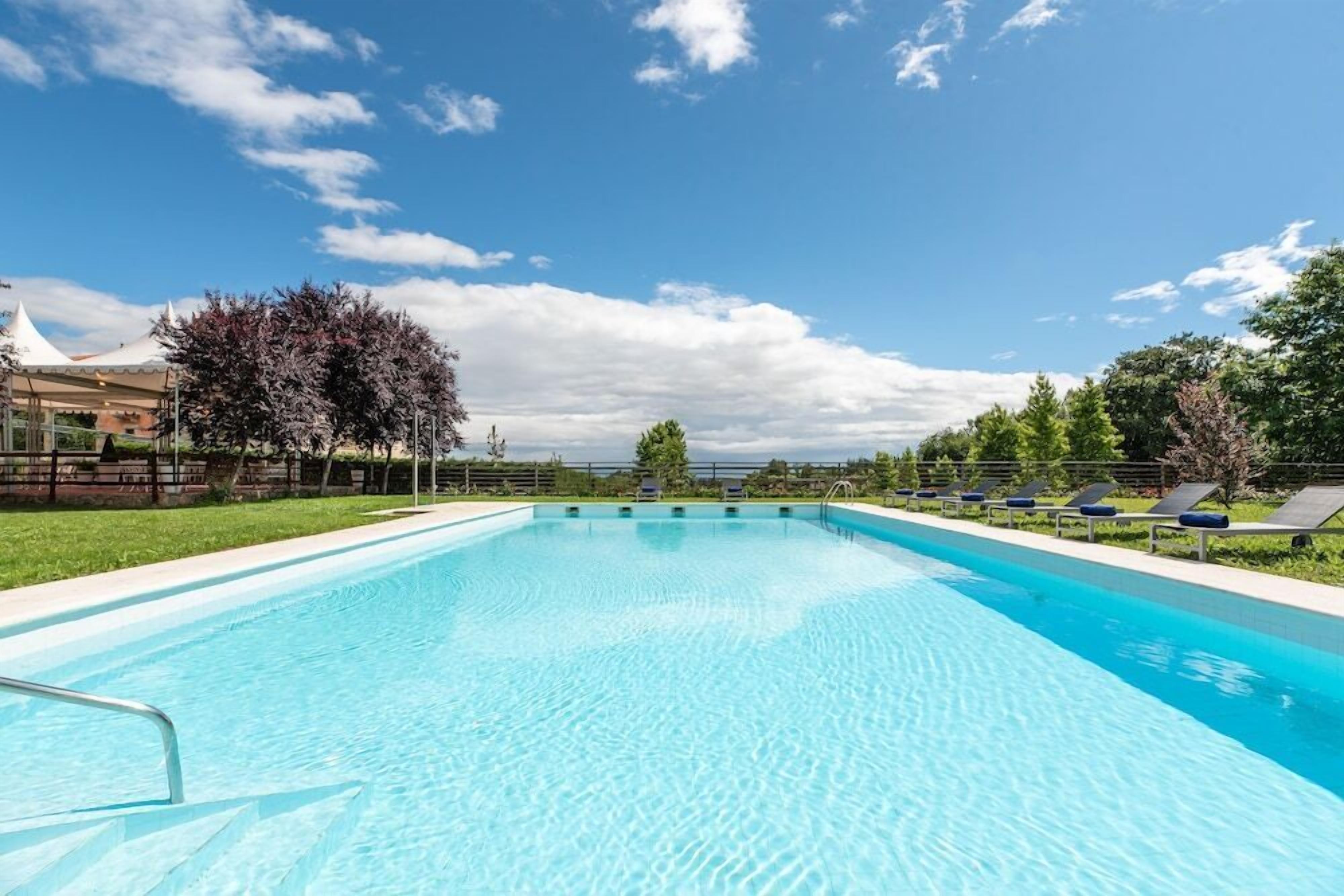 A rectangular swimming pool with clear blue water, surrounded by a grassy area and trees.