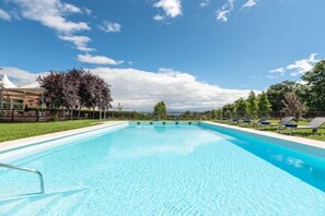 A rectangular swimming pool with clear blue water, surrounded by a grassy area and trees.