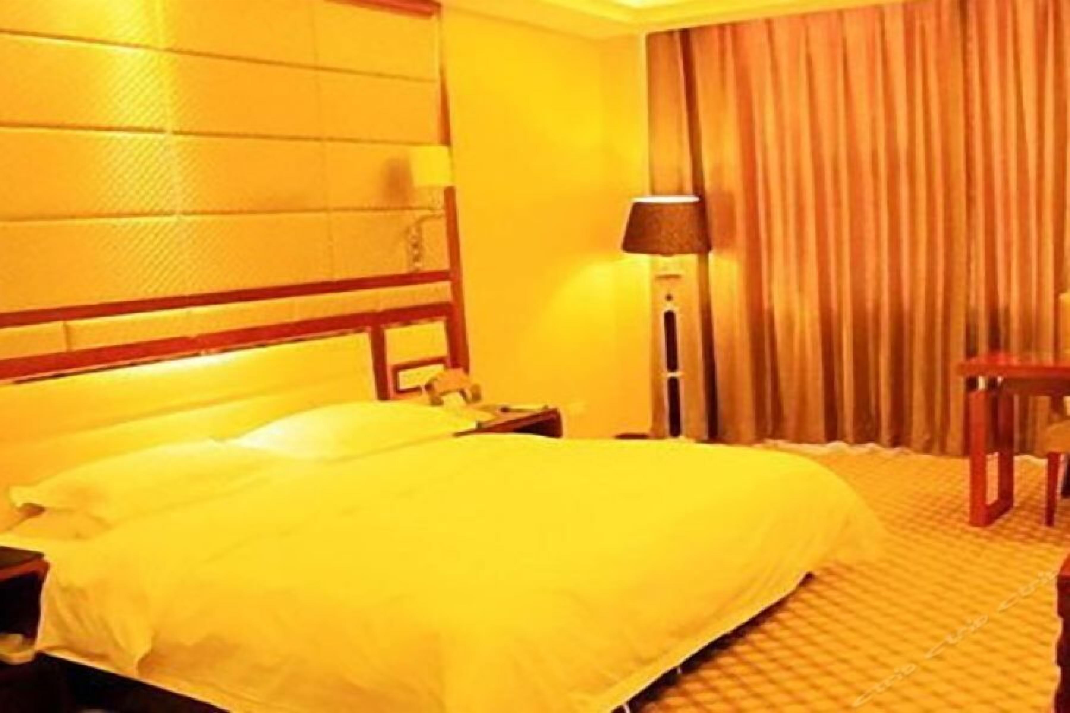Une chambre d’hôtel avec un grand lit, une table de chevet, une lampe et une fenêtre avec des rideaux.