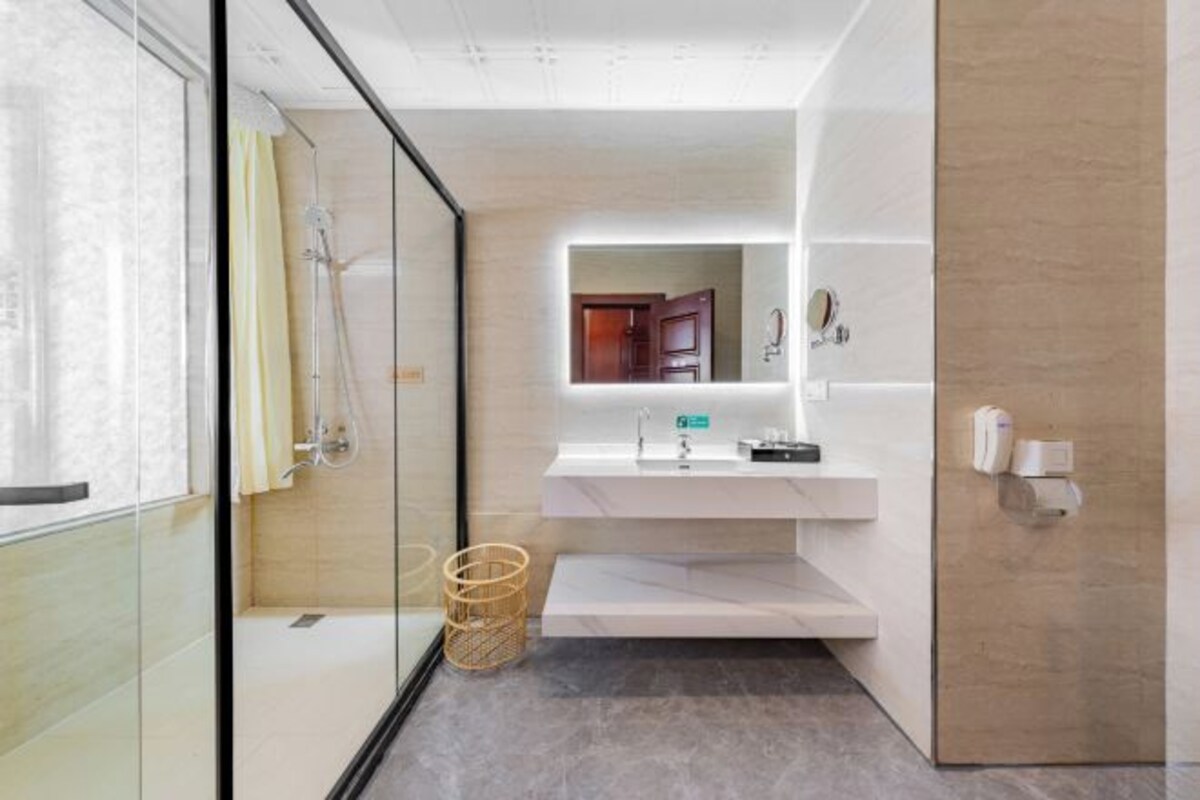 A modern bathroom with a glass shower enclosure, a white sink with a mirror above, and a wooden door.