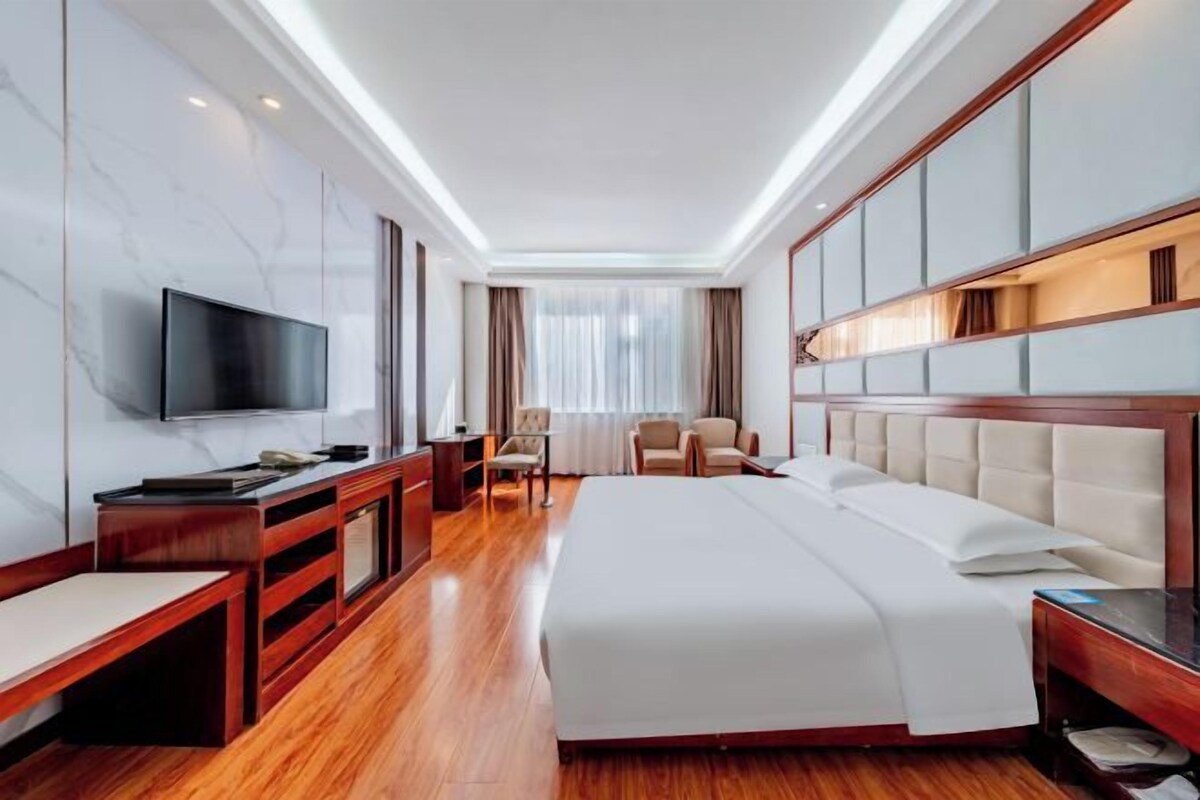 Una habitación de hotel con una cama grande, televisión, escritorio y silla.