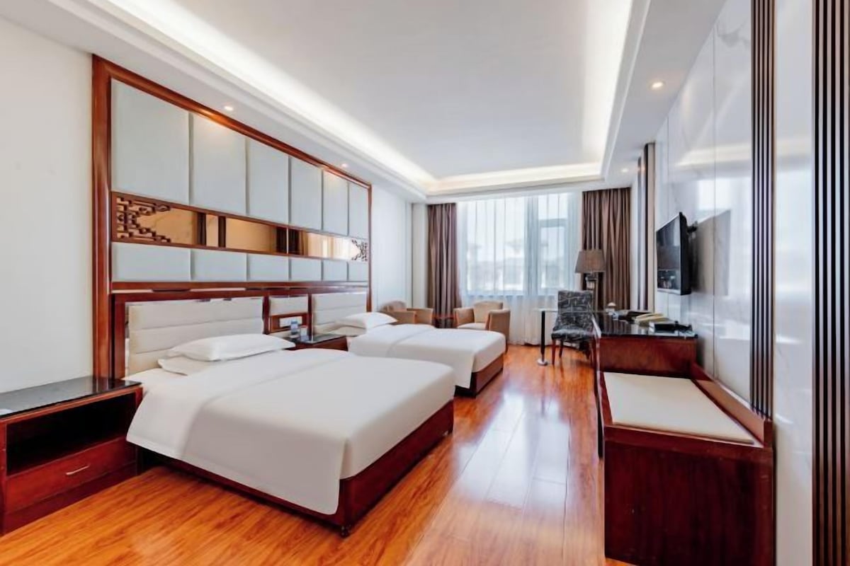 A hotel room with two beds, a desk, a chair, and a large mirror.