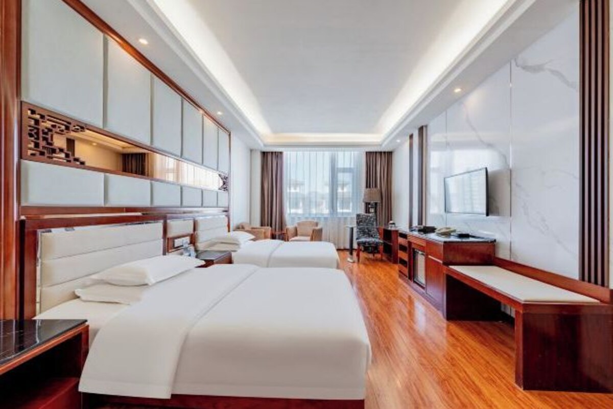 A hotel room with two beds, a desk, a chair, a TV, and a window.