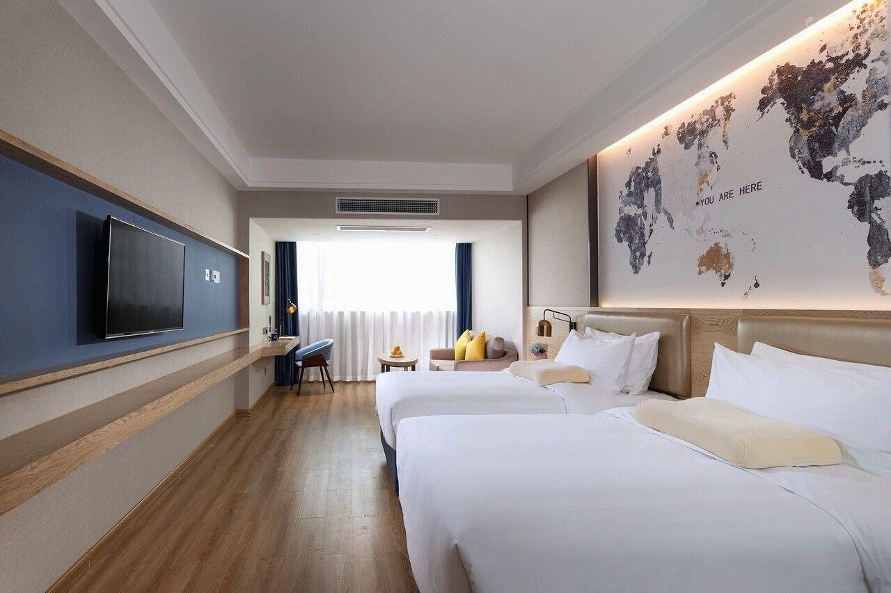 A hotel room with two beds, a TV, a desk, and a world map on the wall.