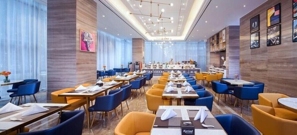 Un espacioso comedor de hotel con varias mesas y sillas, una larga barra y un candelabro.