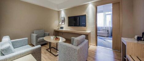 A modern living room with grey sofas, a round coffee table, and a flat-screen TV mounted on the wall.