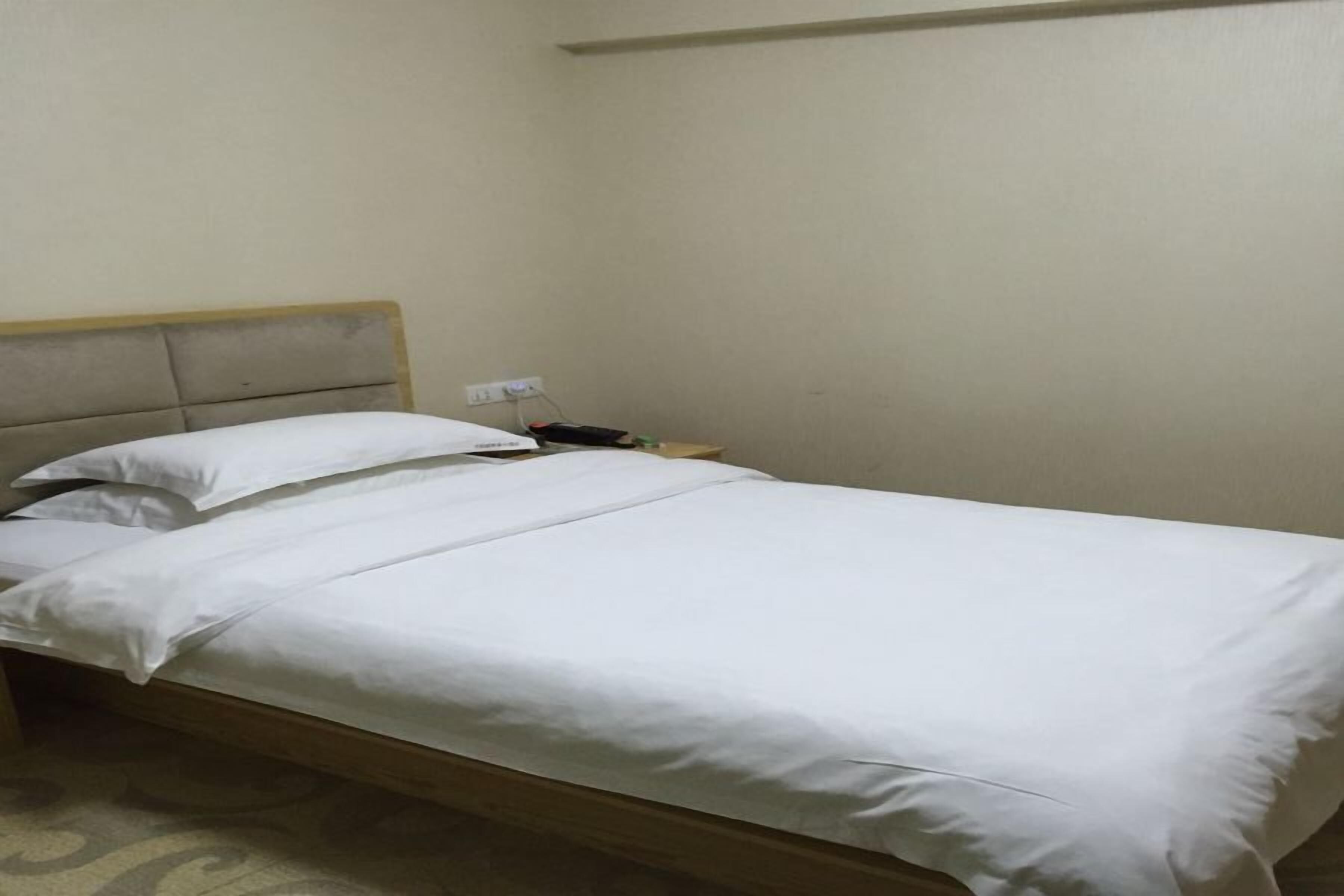 Una cama individual con ropa de cama blanca en una habitación con pared lisa y cabecera de madera.