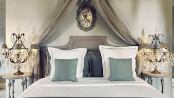 Un dormitorio con cama a dosel, dos mesitas de noche con lámparas y un espejo decorativo sobre la cama.