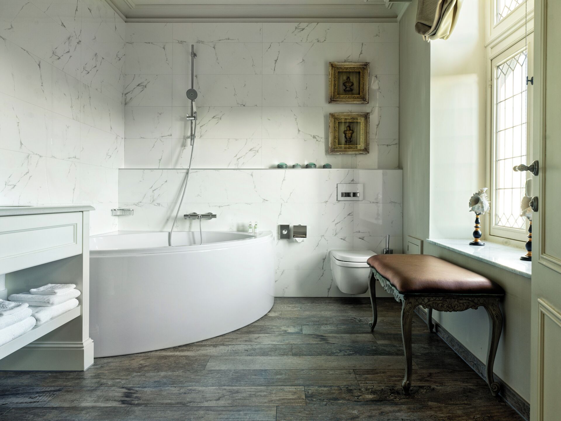 A bathroom with a freestanding bathtub, a toilet, a bench, and framed pictures on the wall.