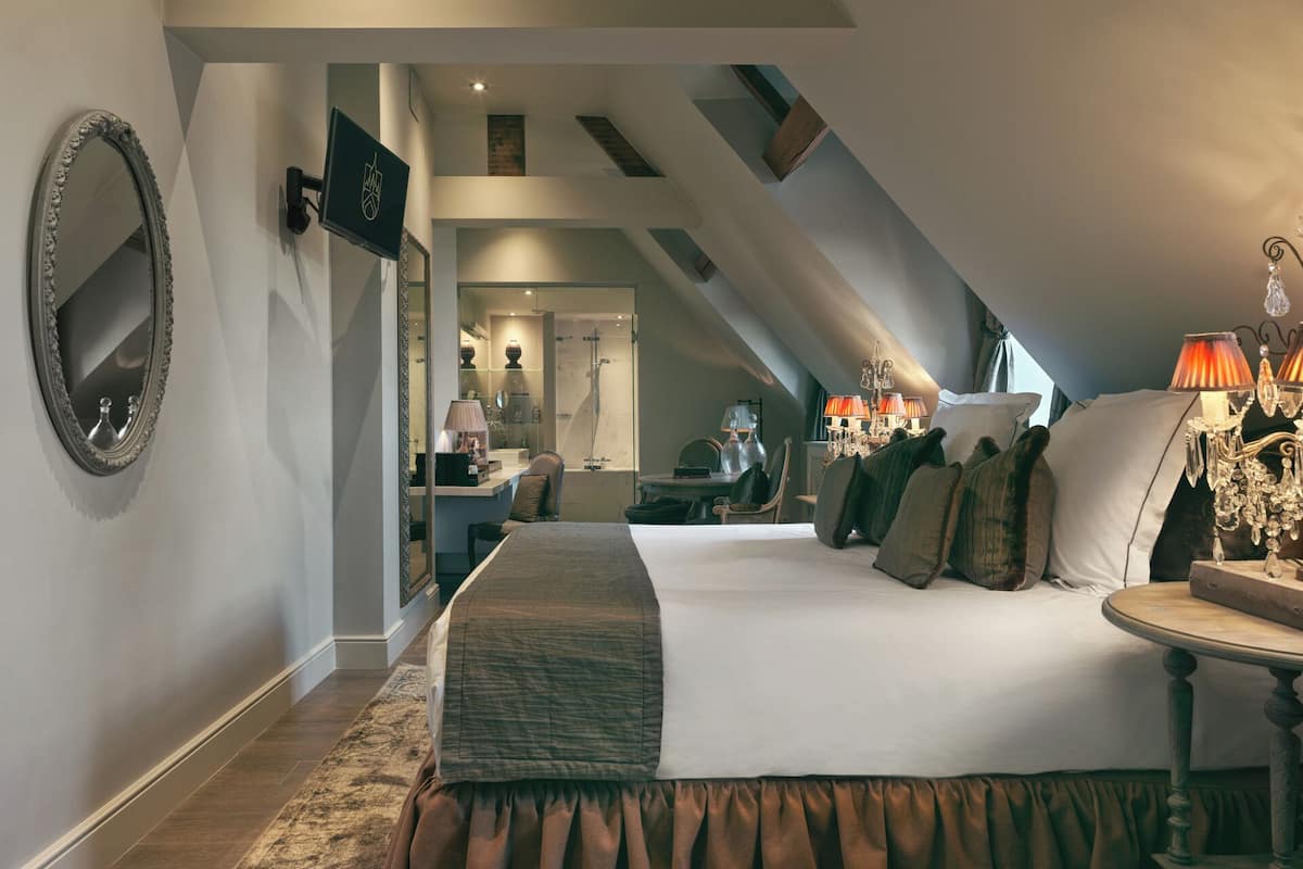 A bedroom with a large bed, a mirror, a desk, and a chandelier.