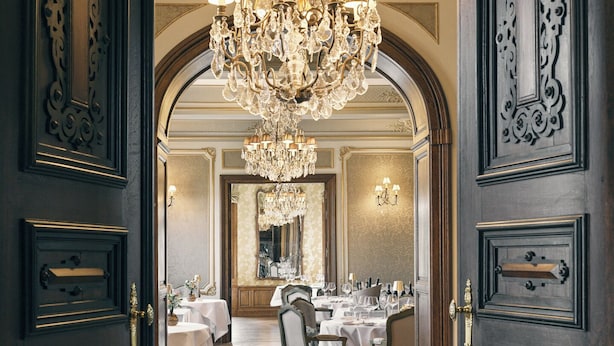 Un elegante comedor con una araña, puertas de madera y un muro espejado.
