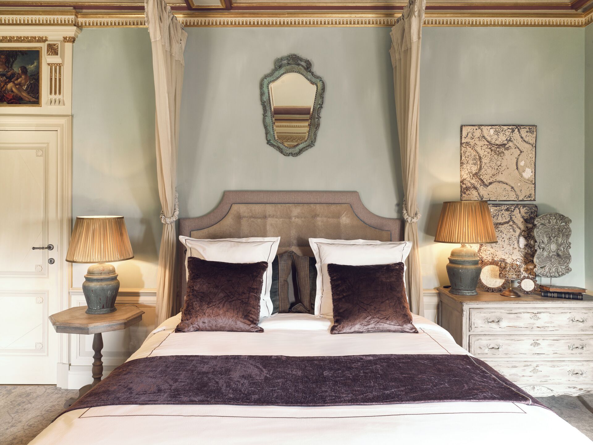 A bedroom with a four-poster bed, two bedside lamps, a mirror, and a decorative piece on the wall.