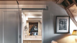 Un dormitorio acogedor en el ático, con techo de madera, una puerta blanca, un escritorio pequeño con lámpara y un cuadro en la pared.