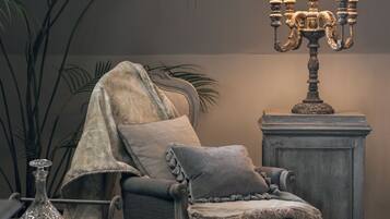 A chair with a blanket, a lamp, and a plant in a room with a patterned carpet.