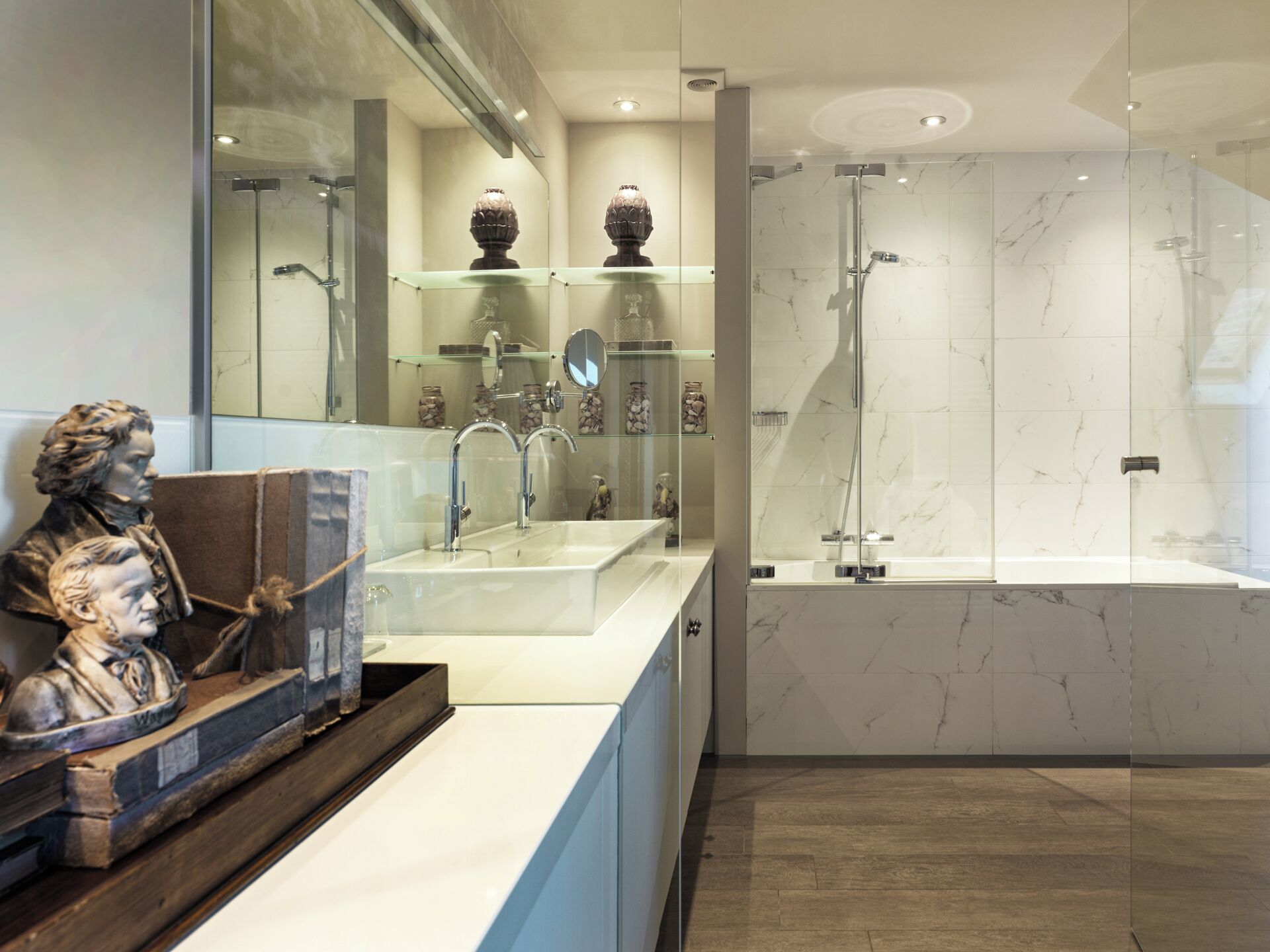 A modern bathroom with a glass shower enclosure, a marble-tiled shower area, and a vanity with a glass shelf displaying decorative items.