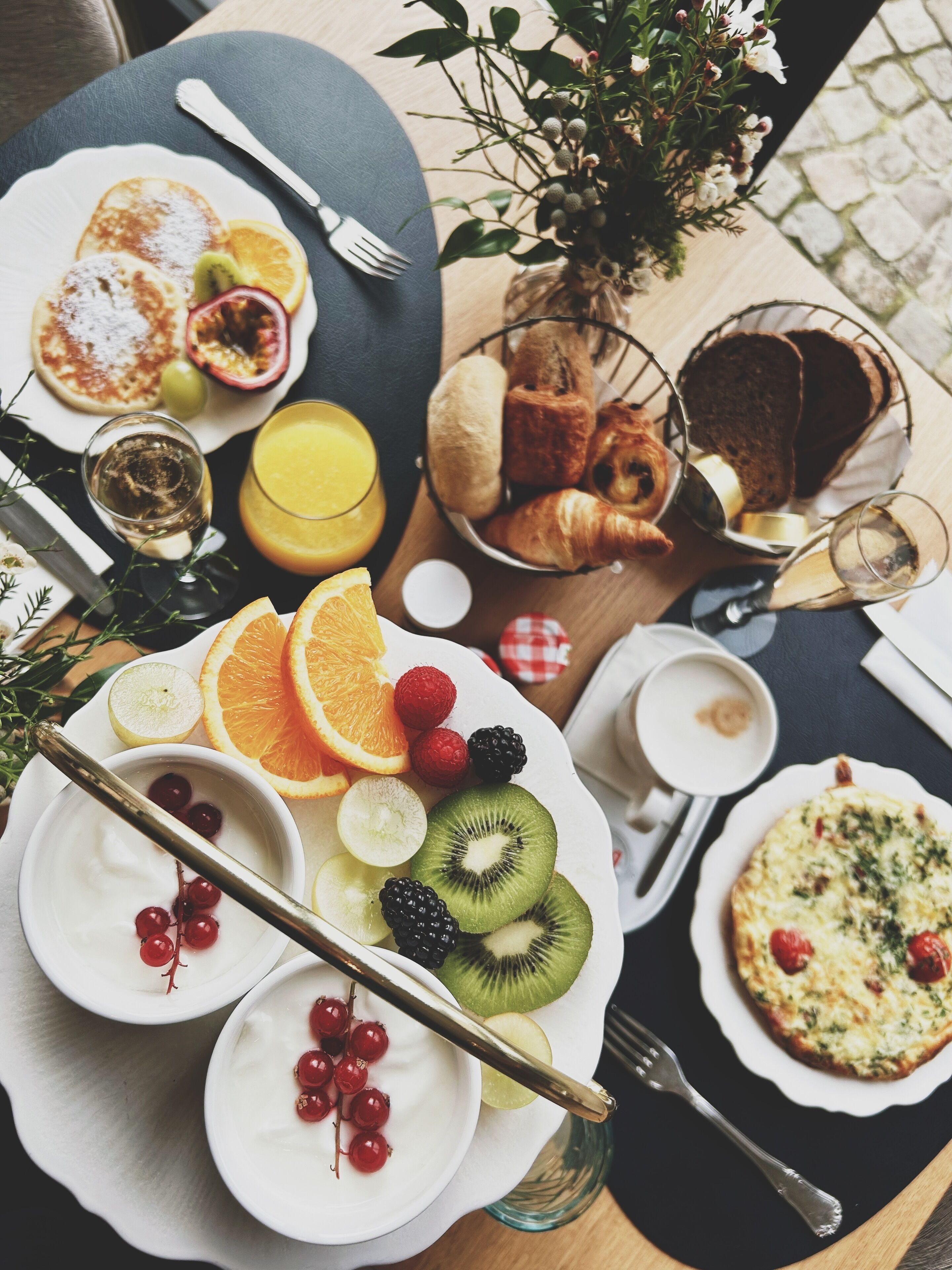 A breakfast setting with plates of pancakes, pastries, and a fruit bowl.