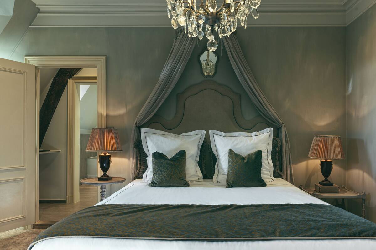 A bedroom with a large bed, two bedside tables with lamps, a chandelier, and a mirror on the wall.