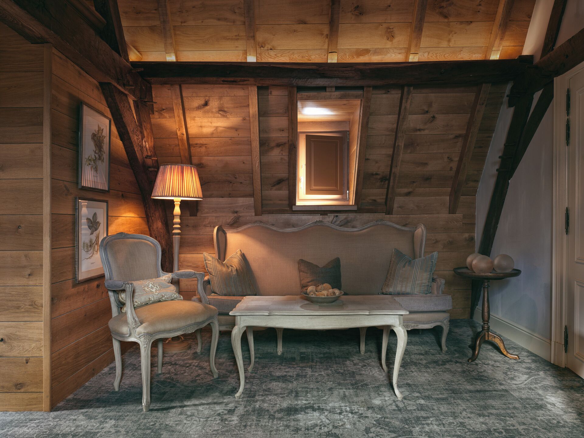 Um quarto aconchegante com paredes de madeira, um sofá, uma poltrona, uma mesa e uma luminária.