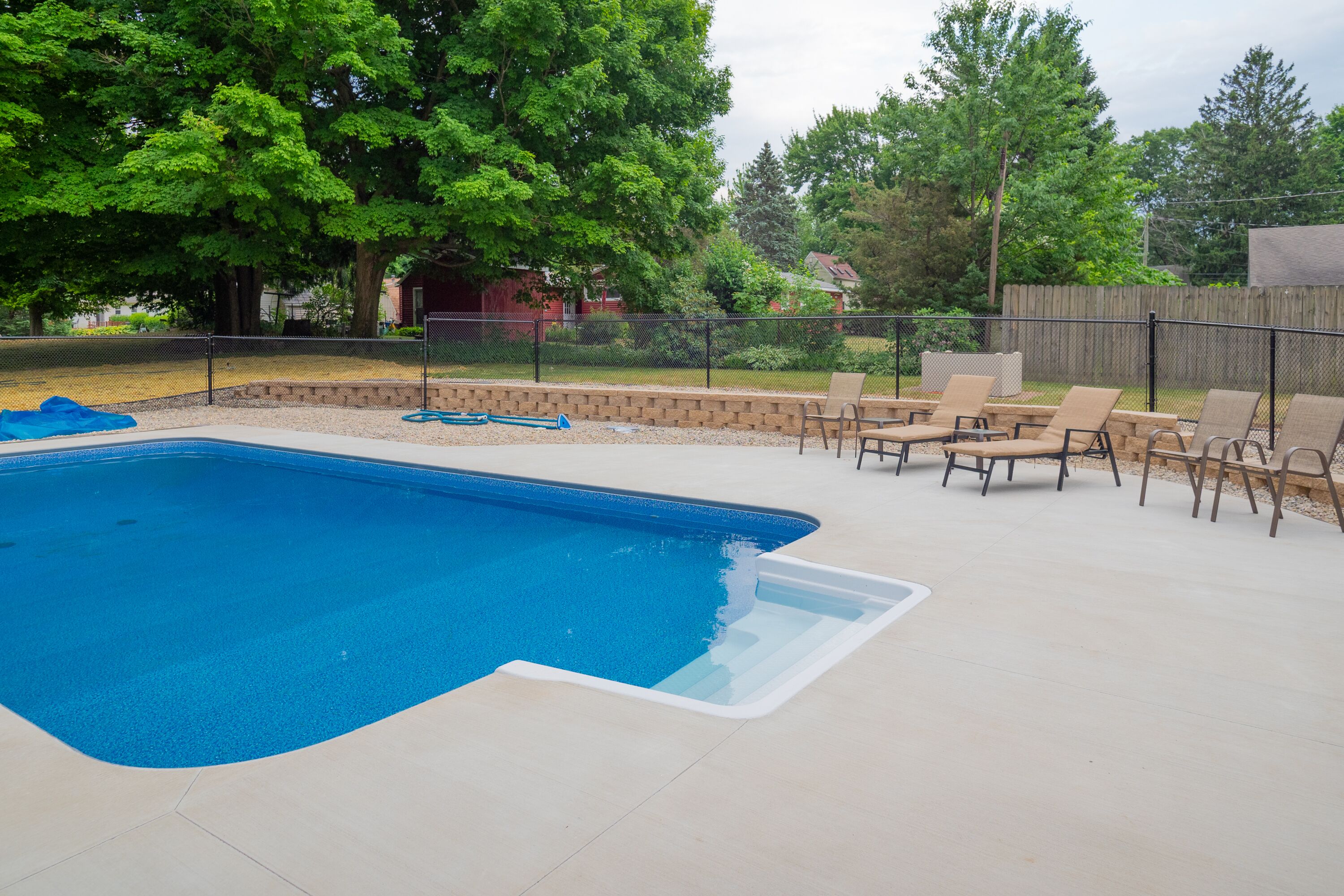 A backyard with a swimming pool, outdoor furniture, and a wooden fence.