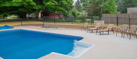 A backyard with a swimming pool, outdoor furniture, and a wooden fence.