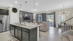 Een moderne keuken met een centraal eiland, inbouwapparatuur, hanglampen en een eetgedeelte met een trap.