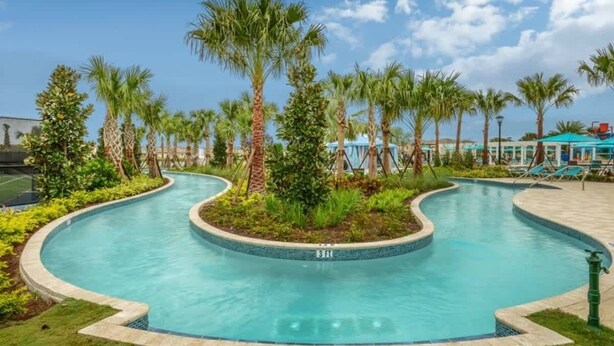 A swimming pool with a curved design, surrounded by palm trees and a covered area with chairs. - 5BD Windsor Westside Private Pool (WW 8920) (Kissimmee)