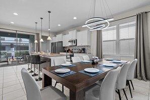 A modern kitchen with white cabinets, a built-in microwave, and a dining area with a wooden table set for four. - 5BD Windsor Westside Private Pool (WW 8920) (Kissimmee)