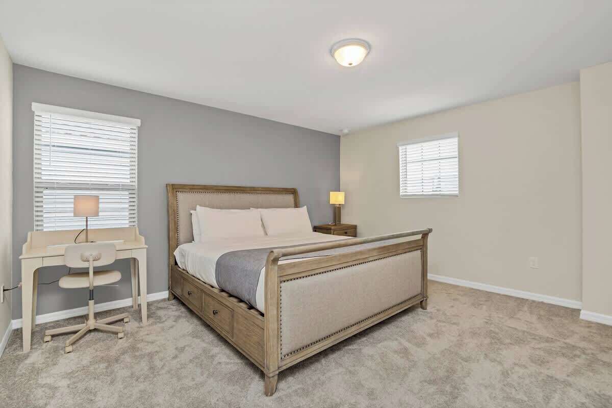 A bedroom with a bed, desk, chair, and two bedside lamps.