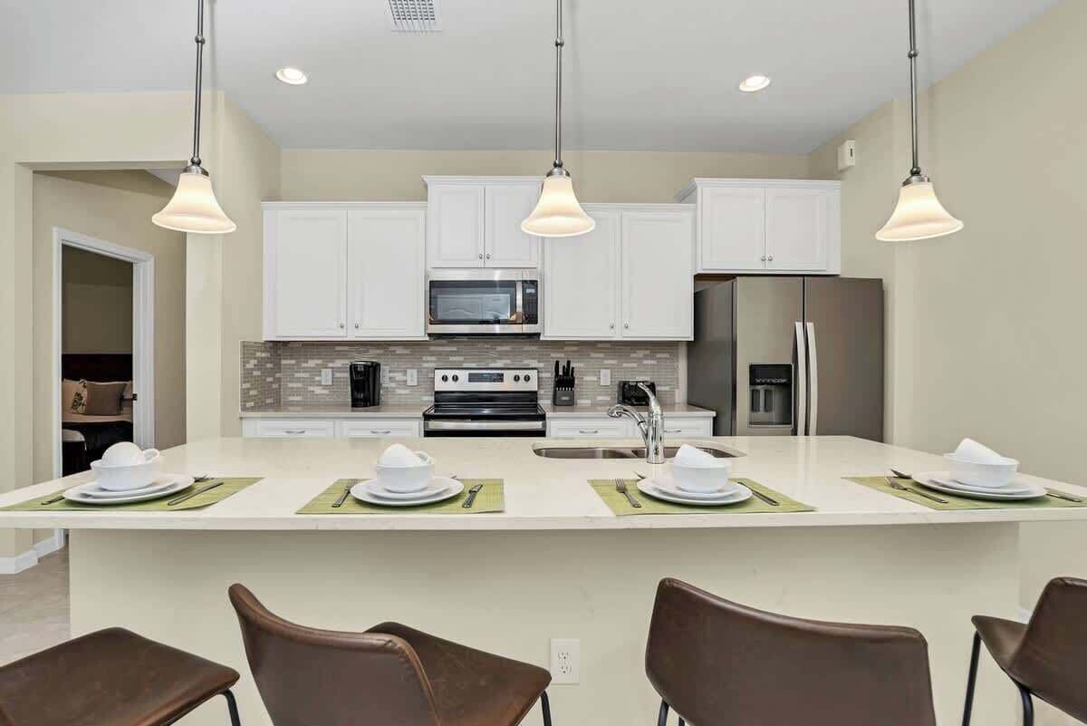 A modern kitchen with white cabinets, a central island with seating, and pendant lighting.