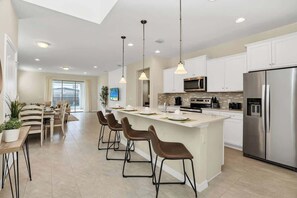 Une cuisine moderne dotée d’un îlot central, d’appareils électroménagers en acier inoxydable et de luminaires suspendus.