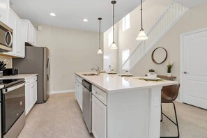 A modern kitchen with white cabinetry, stainless steel appliances, pendant lighting, and a central island.