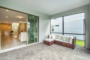 A modern living area with a sectional sofa, a glass sliding door leading to a dining area, and large windows.
