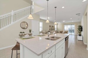 A modern kitchen with a central island, a dining area, and a staircase leading to an upper level.