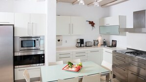 A modern kitchen with stainless steel appliances, white cabinetry, and a dining area with a glass table. - Exquisite "Villa Luna" with Pool & Jacuzzi close to the amazing Lia beach! (Mykonos)