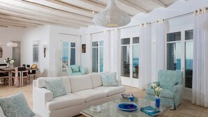 A spacious living room with a white sofa, a teal armchair, and a glass coffee table. - Exquisite "Villa Luna" with Pool & Jacuzzi close to the amazing Lia beach! (Mykonos)