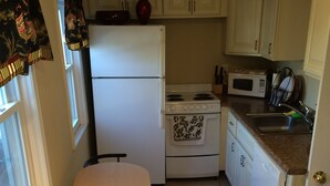 A compact kitchen with a refrigerator, stove, microwave, and a small dining table with two chairs. - Spacious Apt. 2 car free parking great location. (Cambridge)