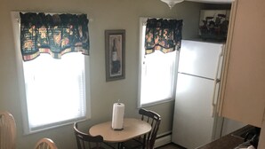 A small kitchen with a dining table, chairs, a refrigerator, and a window with curtains. - Spacious Apt. 2 car free parking great location. (Cambridge)