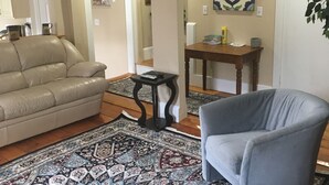 A living room with a beige sofa, a grey armchair, a patterned rug, a wooden coffee table, and a decorative wall piece. - Spacious Apt. 2 car free parking great location. (Cambridge)