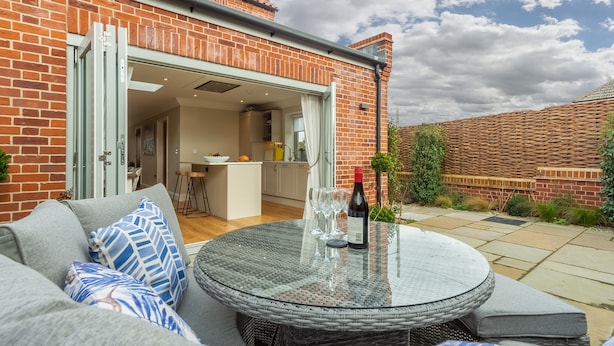 Une terrasse avec une table ronde, des sièges d’extérieur et une bouteille de vin.