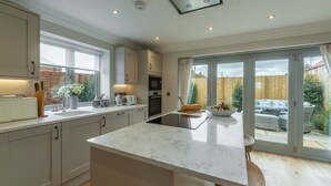 Une cuisine moderne dotée d’un îlot central, d’appareils électroménagers intégrés et de grandes portes-fenêtres coulissantes donnant sur un jardin.