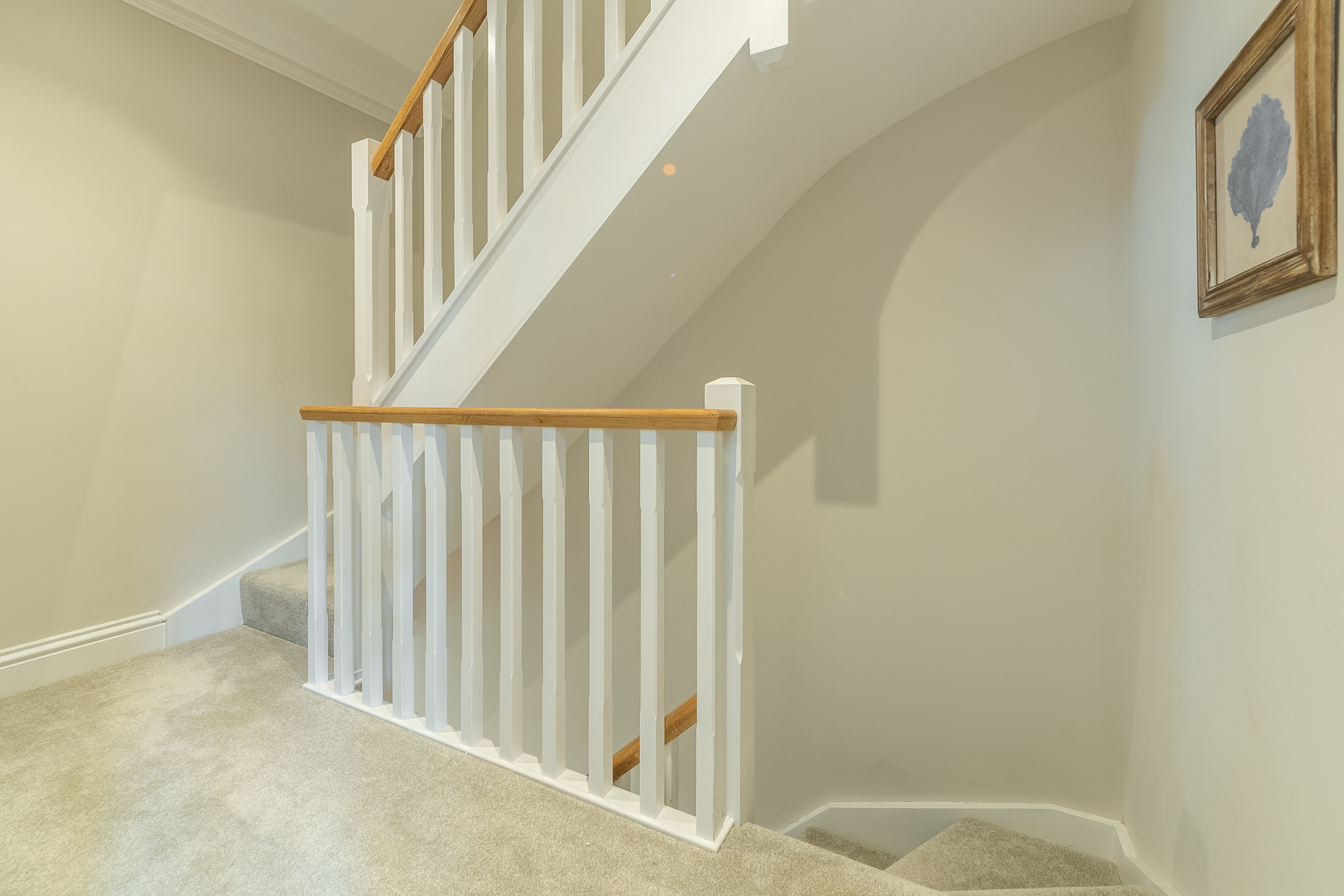 Eine Treppe mit weißen Geländern, einem Holzhandlauf, Teppichstufen und einem gerahmten Bild an der Wand.