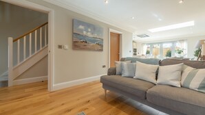 Un salon spacieux doté d’un plancher en bois, d’un canapé gris avec des coussins à rayures, d’un tableau accroché au mur et d’un escalier menant à une autre pièce.