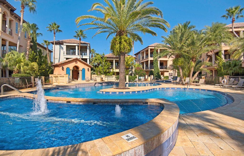 A pool area with a fountain, surrounded by palm trees and buildings with balconies.