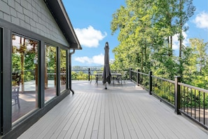 A wooden deck with a railing, a statue, and a view of trees and mountains. - Blue Ridge Bliss | Mountain Home with Hot Tub & Stunning Views! (Weaverville)