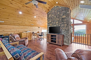 A wooden interior with a stone fireplace, a flat-screen TV, leather furniture, and a view through large windows. - Blue Ridge Bliss | Mountain Home with Hot Tub & Stunning Views! (Weaverville)