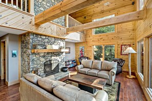 A spacious living area with a stone fireplace, wooden beams, and a high ceiling.