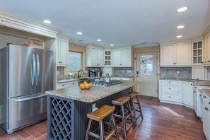 A modern kitchen with a stainless steel refrigerator, granite countertops, and wooden stools. - Blue Ridge Bliss | Mountain Home with Hot Tub & Stunning Views! (Weaverville)